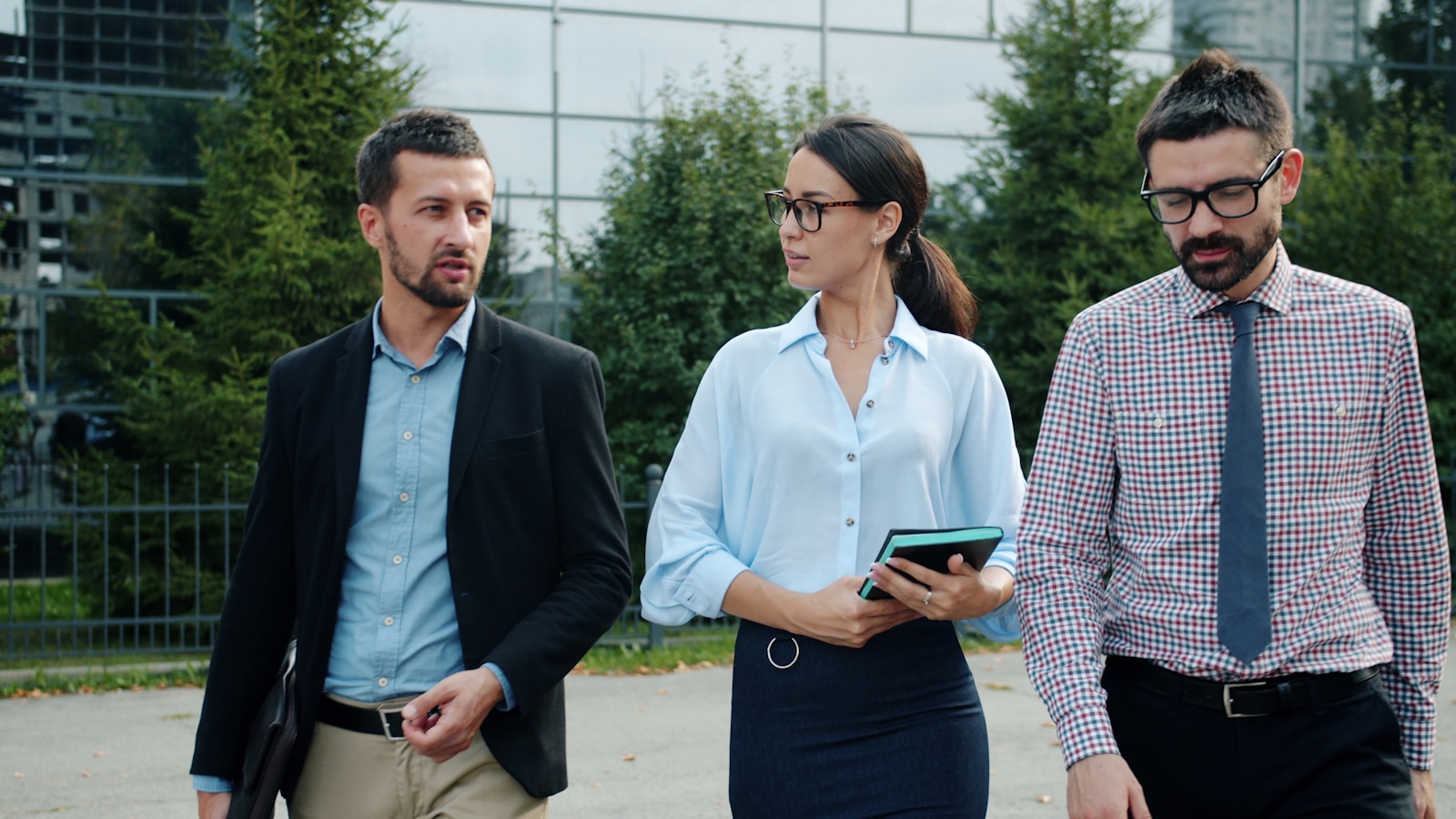 Three colleagues walking and talking outside a glass office building