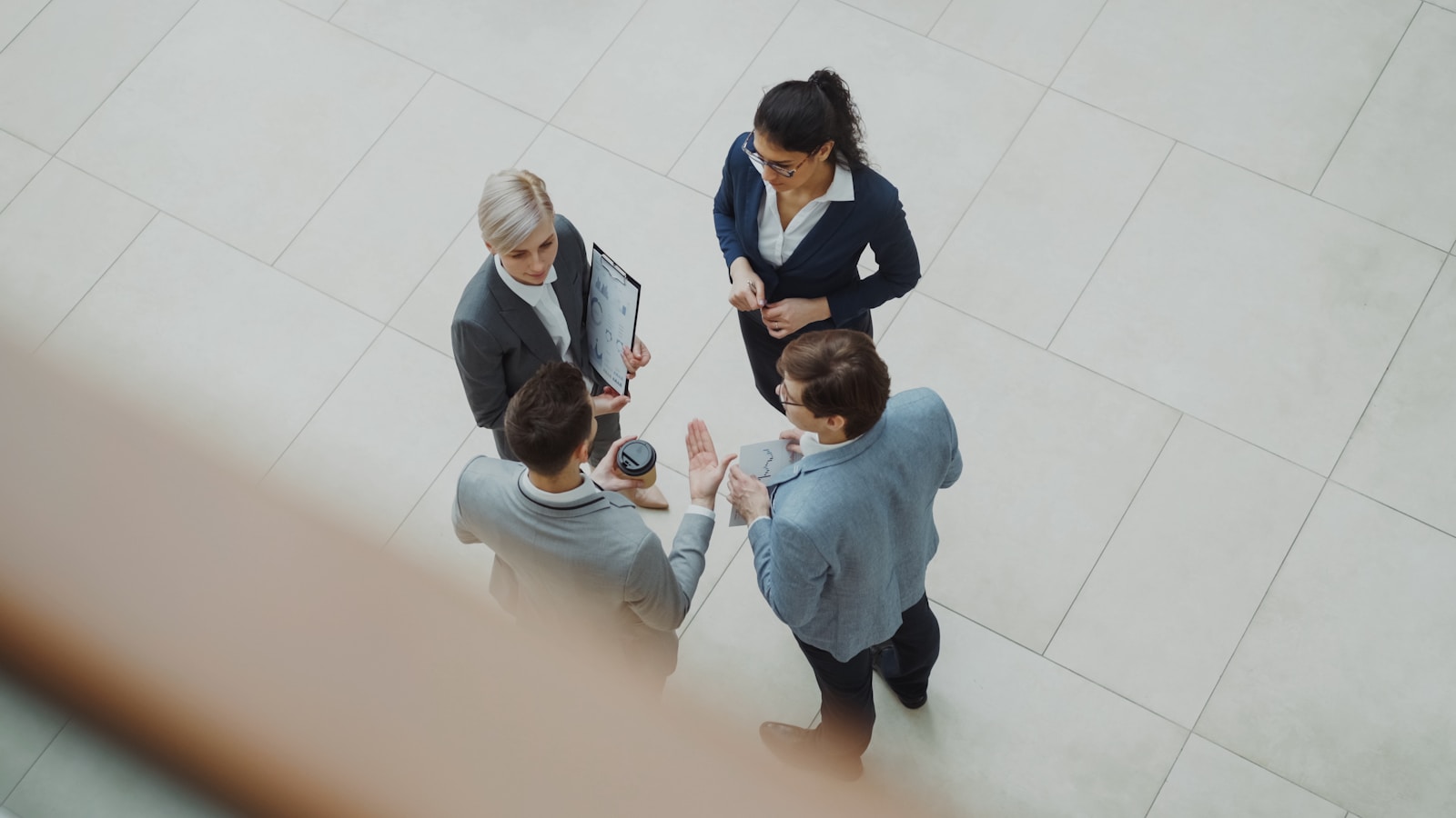Overhead view of four managers in a standing huddle reviewing notes in an office atrium